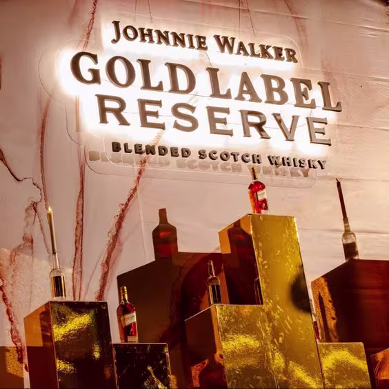 La imagen muestra varias botellas del whisky Johnnie Walker Gold Label Reserve y un cartel luminoso que dice: Johnnie Walker Gold Label Reserve Blended Scotch Whisky.