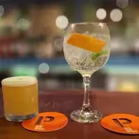 En la imagen se ven dos cócteles sobre una barra de madera. En el lado izquierdo un vaso pequeño. Y del lado derecho un copón.