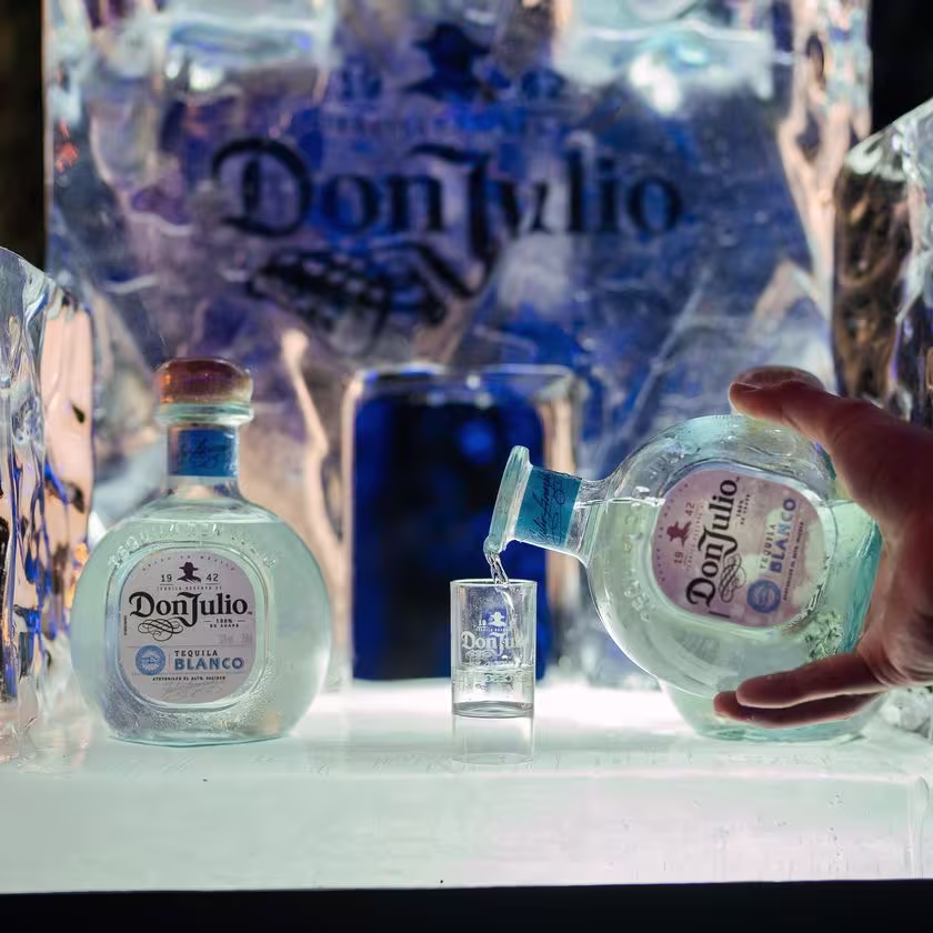 En la imagen se ven dos botellas de Don Julio Blanco. Una de ellas esta sirviendo en un vaso pequeño.