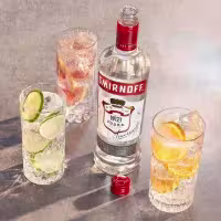 La imagen muestra una botella de vodka Smirnoff N°21 junto a tres vasos decorados con distintas frutas.