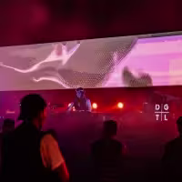 La imagen muestra una vista panorámica de la fiesta con una dj y el público grande enfrente de ella
