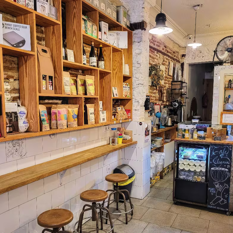 Estanterías de madera repletas de productos artesanales y taburetes altos en Ruda Café, un espacio cálido con ladrillo visto y detalles cuidados.