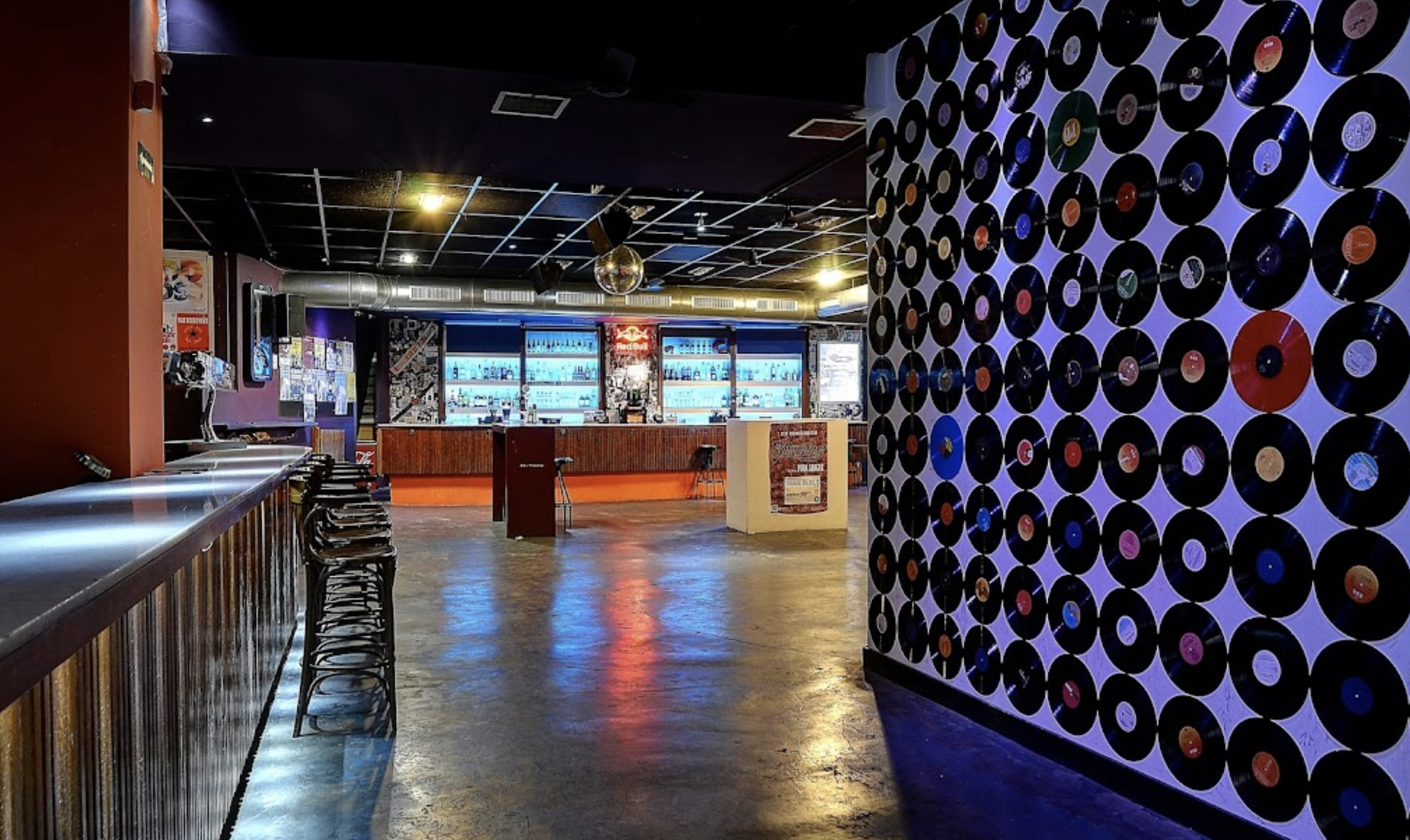 Loco Club, una sala underground con estética retro, barra iluminada y una pared de vinilos, ideal para conciertos y sesiones de DJ.