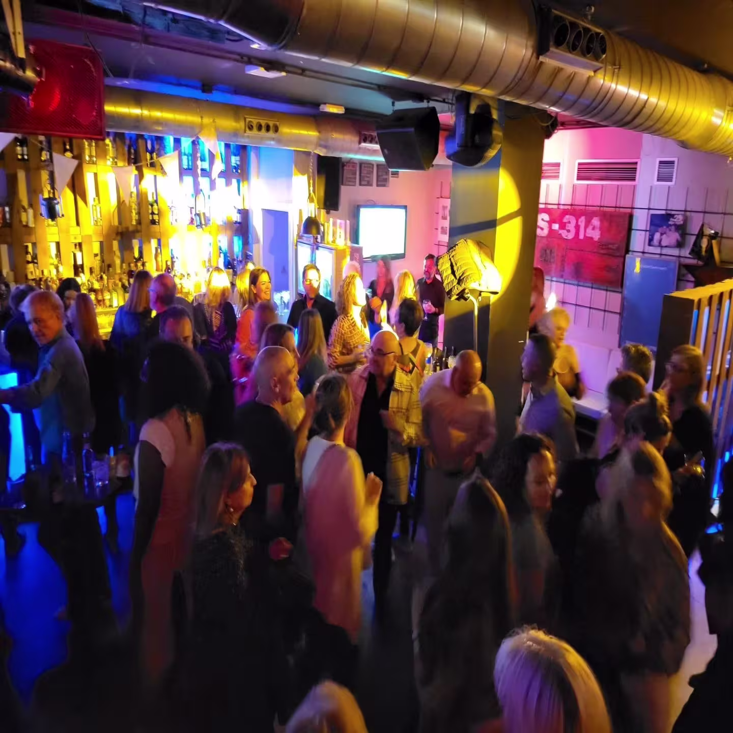 Quitapenas: Ambiente animado en una noche de fiesta, con personas disfrutando de música y luces vibrantes en tonos azules y amarillo"