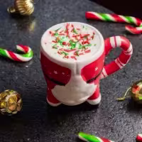 En la imagen se ve una taza con cuerpo de santa claus, decorada con chispas de color verde y rojo, y dulces para decorar.