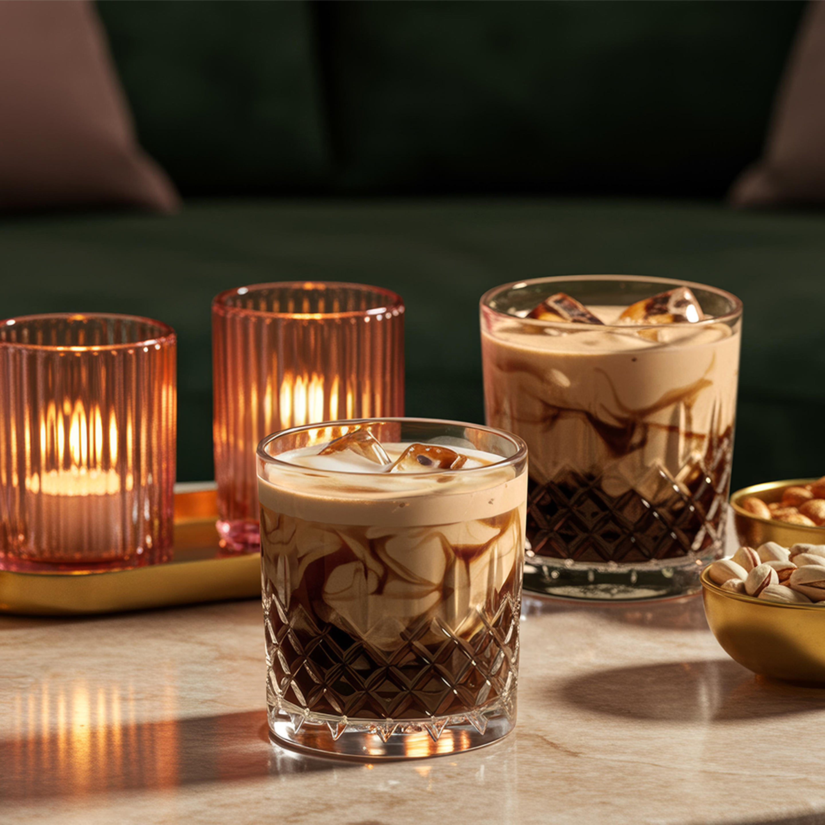 Two White Russians on a shiny marbled table, next to two cosy tea lights and a copper bowl of nuts.
