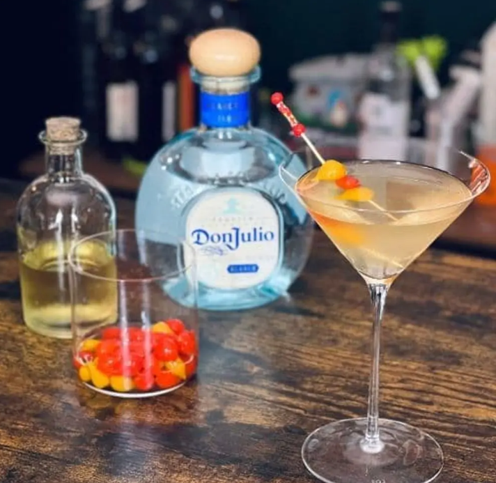 En la foto se ve la botella de Don Julio Blanco, una copa con el trago. Acompañan un vaso con ajíes y un tarro pequeño de aceite.