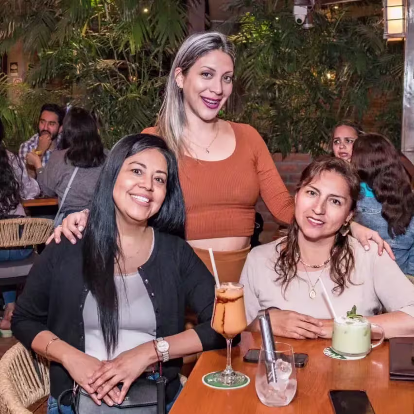 Tres mujeres posando para una foto con tragos en la mesa