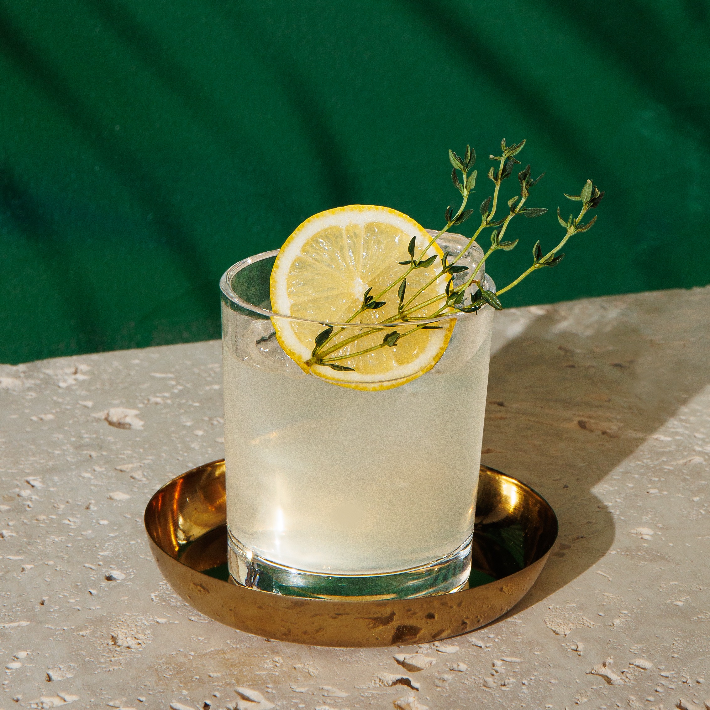 A light yellow cocktail in a rocks glass with ice and a garnish of a lemon wheel and thyme sprig