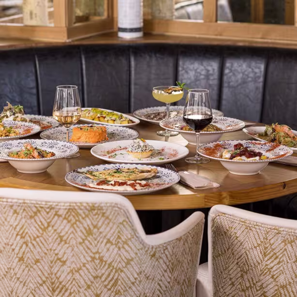 La foto muestra una mesa redonda en Casa Berrinche. Llena de varios platos de comida. Hay platos que parecen contener ensaladas, posiblemente con verduras y hortalizas, y otros platos que podrían ser platos principales con carnes y guarniciones.