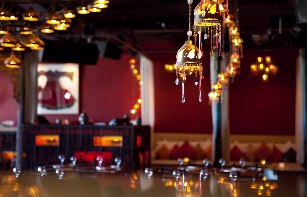 Un interior elegante en CDLC Barcelona, con lámparas doradas de estilo oriental, cojines vibrantes y una decoración cálida en tonos rojos y dorados.