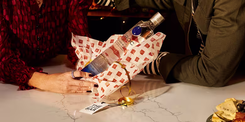 Cîroc vodka being wrapped in branded tissue paper as a gift, surrounded by festive packaging