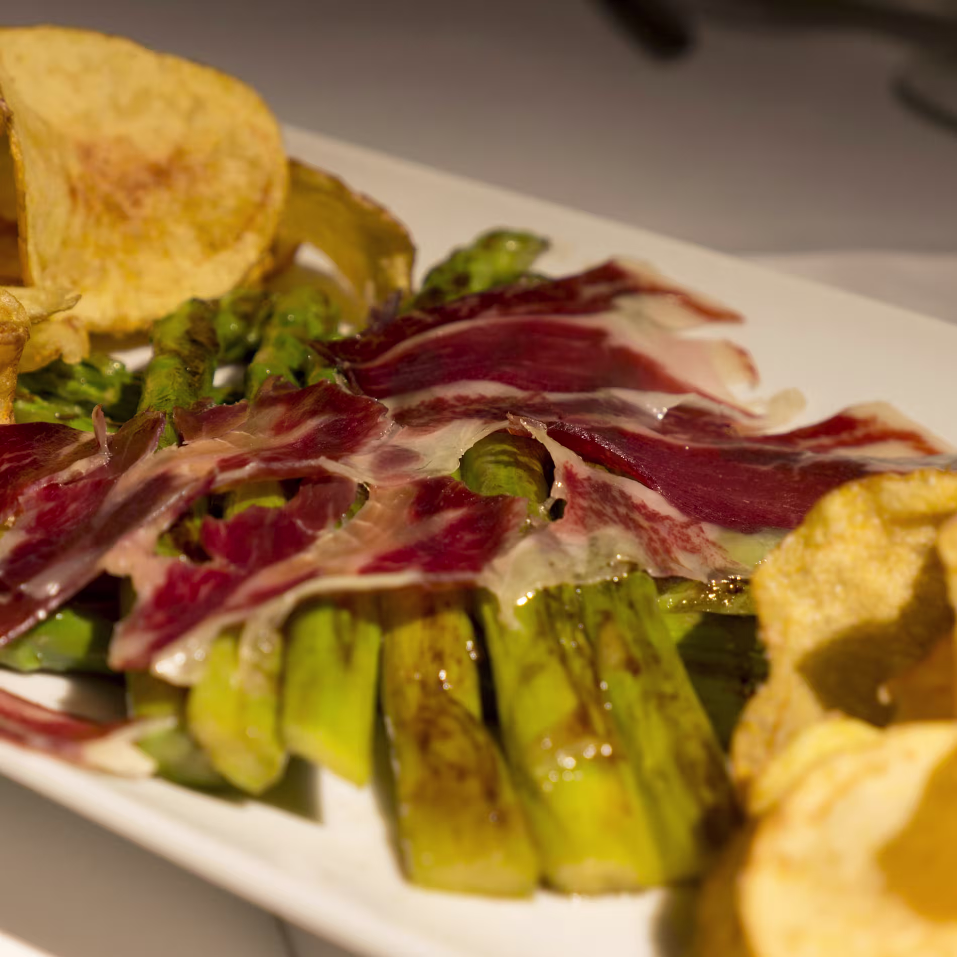 Espárragos verdes a la plancha cubiertos con finas lonchas de jamón ibérico y acompañados de crujientes patatas en Bienmesabe Santa Engracia.