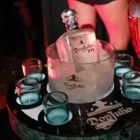 La imagen muestra una botella de Don Julio 70 en una hielera y vasos de shot alrededor.