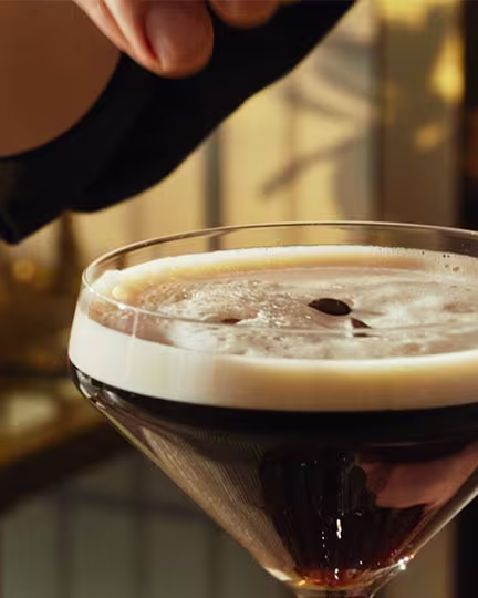 A rum espresso martini being garnished with coffee beans.