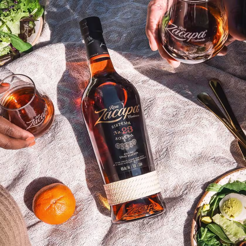 La imagen muestra una botella de ron Zacapa n°23 y dos vasos rellenos con dicho ron.