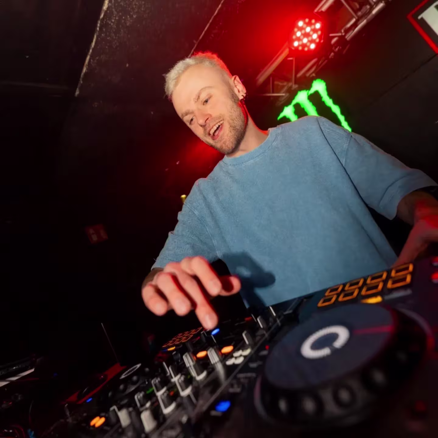 En Rock Star, el DJ domina la cabina con energía y beats potentes bajo luces rojas y el icónico logo de Monster.