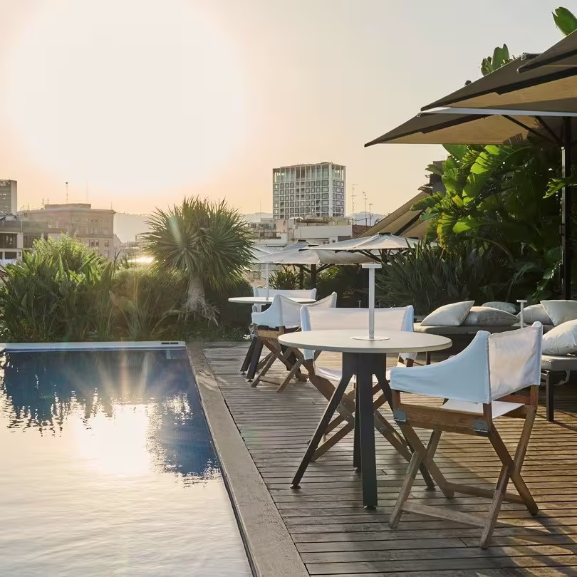 Terraza con piscina, mesas, sombrillas y vistas panorámicas de la ciudad al atardecer en Mood Rooftop Bar, creando un ambiente relajado y moderno.
