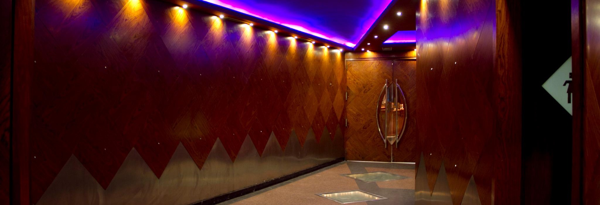 Pasillo iluminado de Kandhavia con diseño elegante, paredes de madera y detalles modernos que conducen a la entrada principal