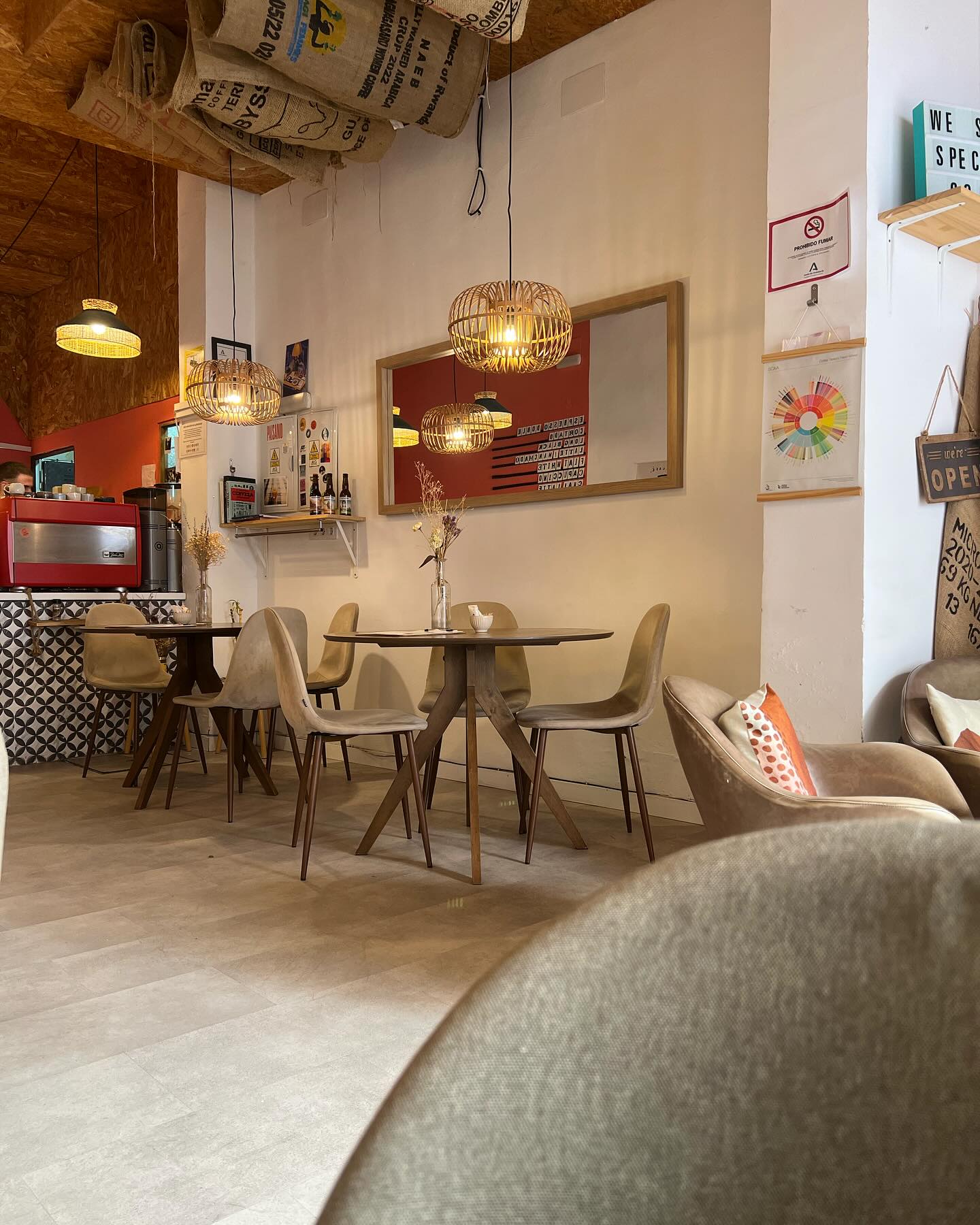 Interior de Purita con mesas de madera, sillas beige, lámparas colgantes de mimbre y decoración acogedora con sacos de café en el techo.
