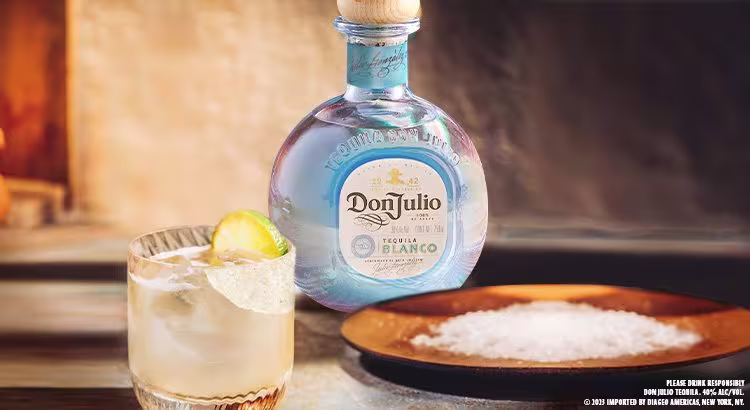 En la imagen se puede apreciar un vaso con el cóctel Margarita. A su lado, se encuentran una botella de tequila Don Julio Blanco y un plato con sal.