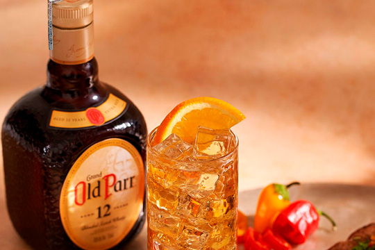 botella de Old Parr junto a cóctel adornado con naranja y chile
