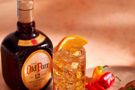 botella de Old Parr junto a cóctel adornado con naranja y chile