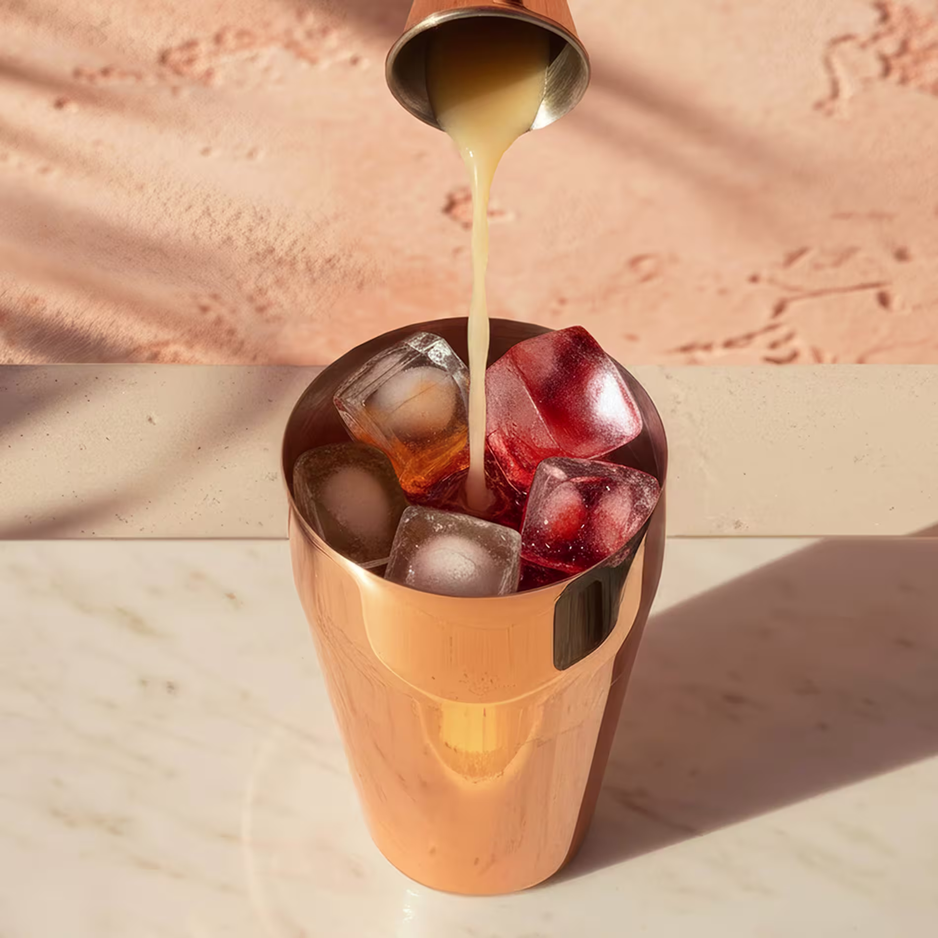 Több színes folyadékot öntenek felülről egy réz koktélkeverőbe.