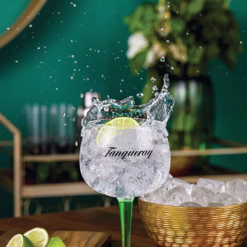 La imagen muestra una copa que contiene un Gin & Tonic, acompañada de otros elementos de coctelería alrededor.