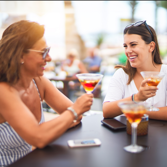 En la imagen se ve dos mujeres, madre e hija. Al aire libre disfrutando de un cóctel.