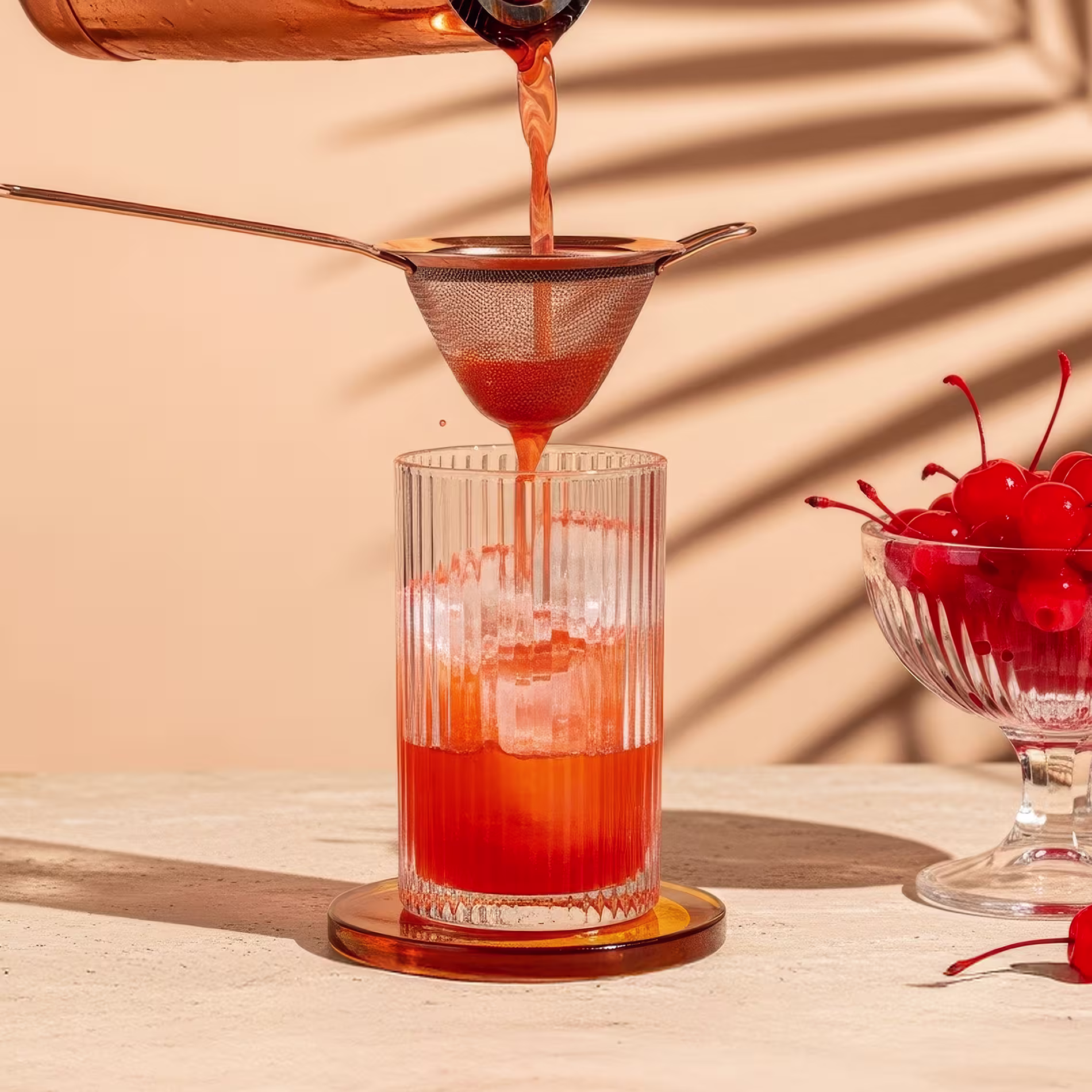 A narancssárga színű Sex on the Beach koktélt egy koktél shakerből egy jéggel teli highball pohárba szűrjük.