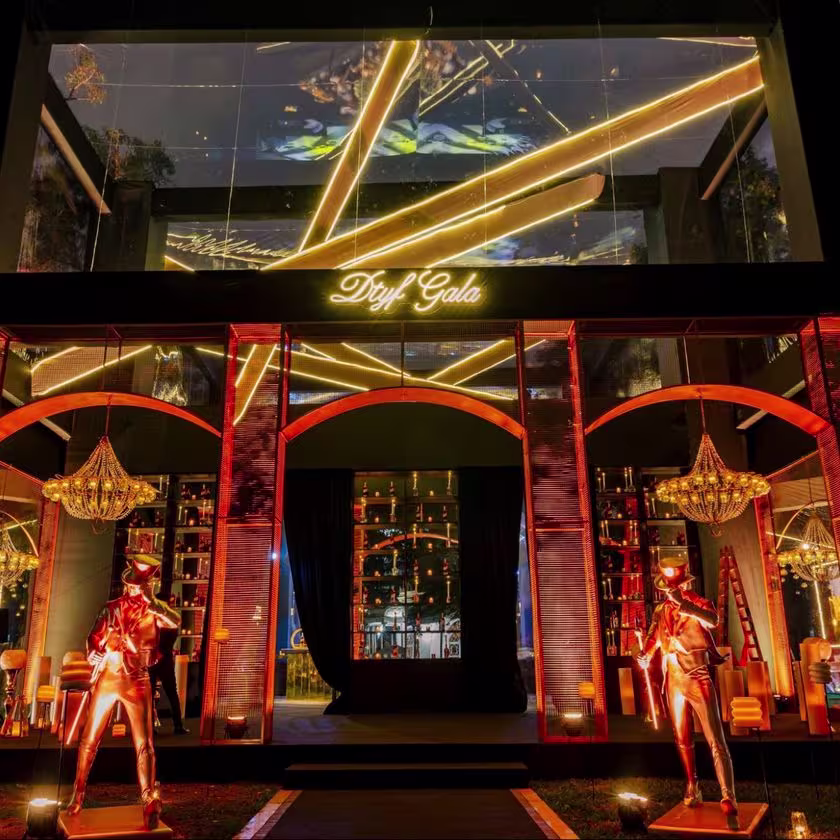 La imagen muestra la entrada de la Gala con un cartel luminoso que dice DTYF Gala, dos estatuas de Johnnie Walker y luces en tonos dorados.