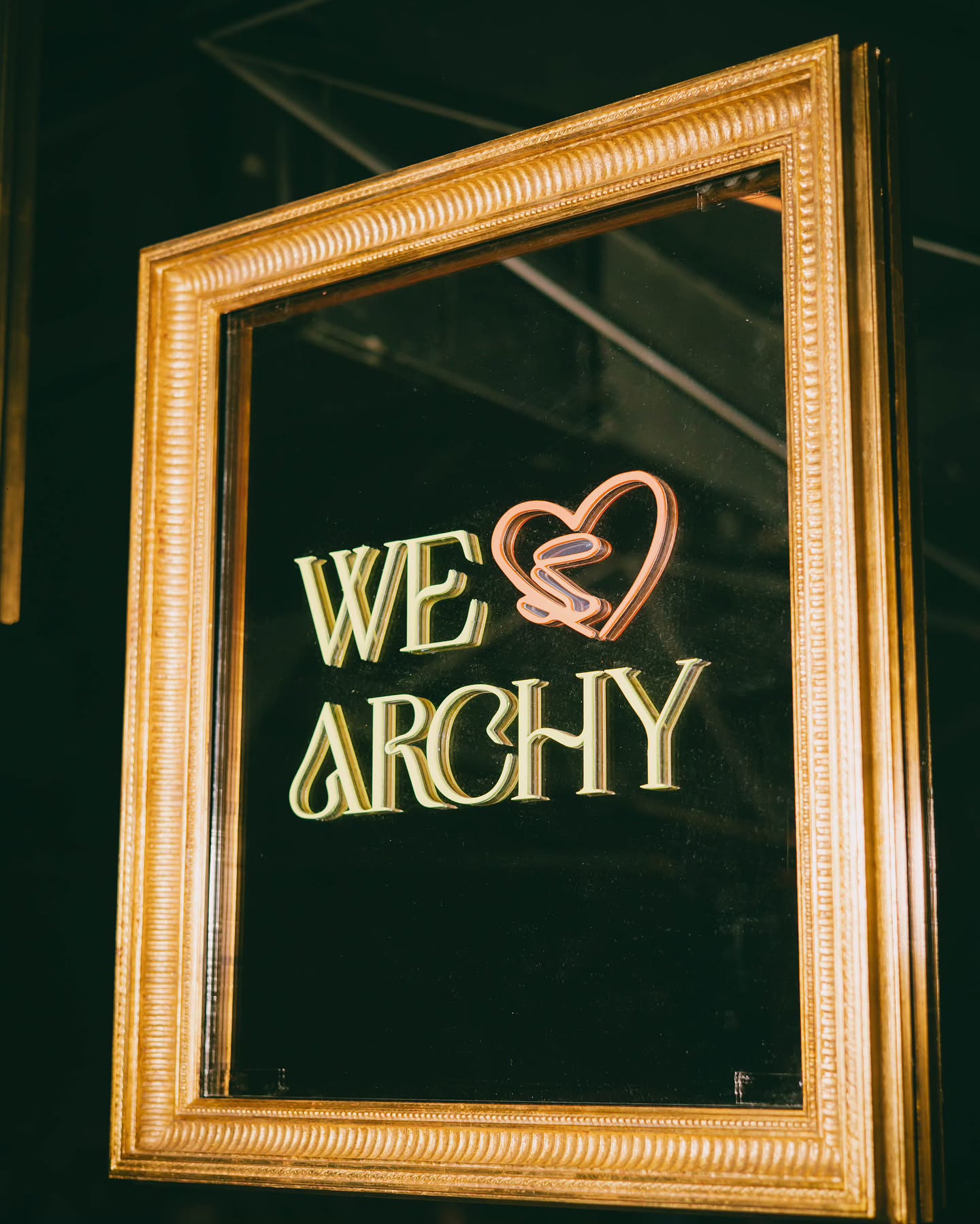 Letrero icónico de Archy enmarcado en dorado, con un diseño luminoso que combina elegancia y modernidad, destacando el lema "We Love Archy"