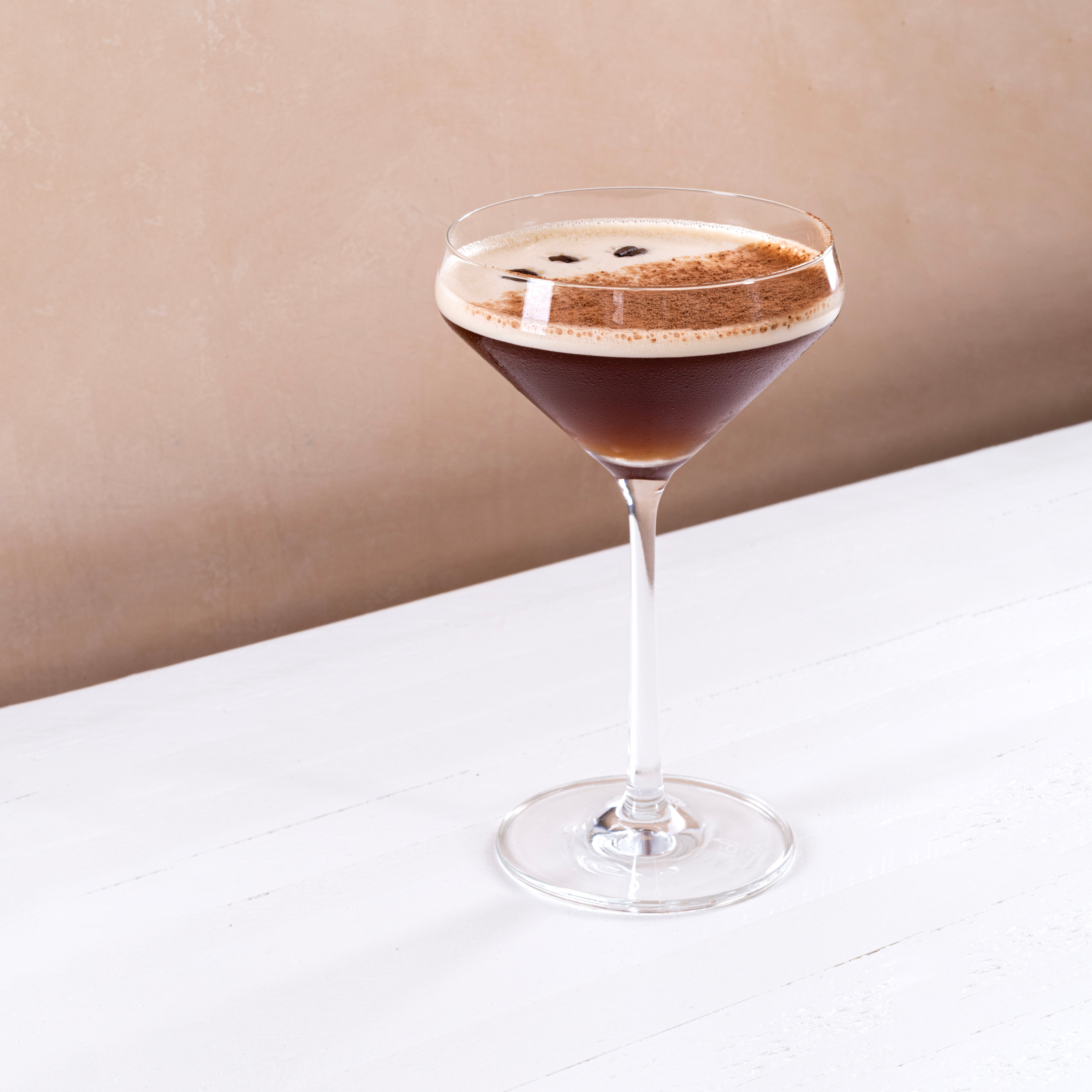 Espresso martini cocktail in a coupe glass garnished with coffee beans on a white table