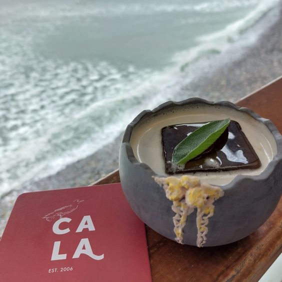 Postre en un plato sobre un posavasos con una playa de fondo. Restobar CALA