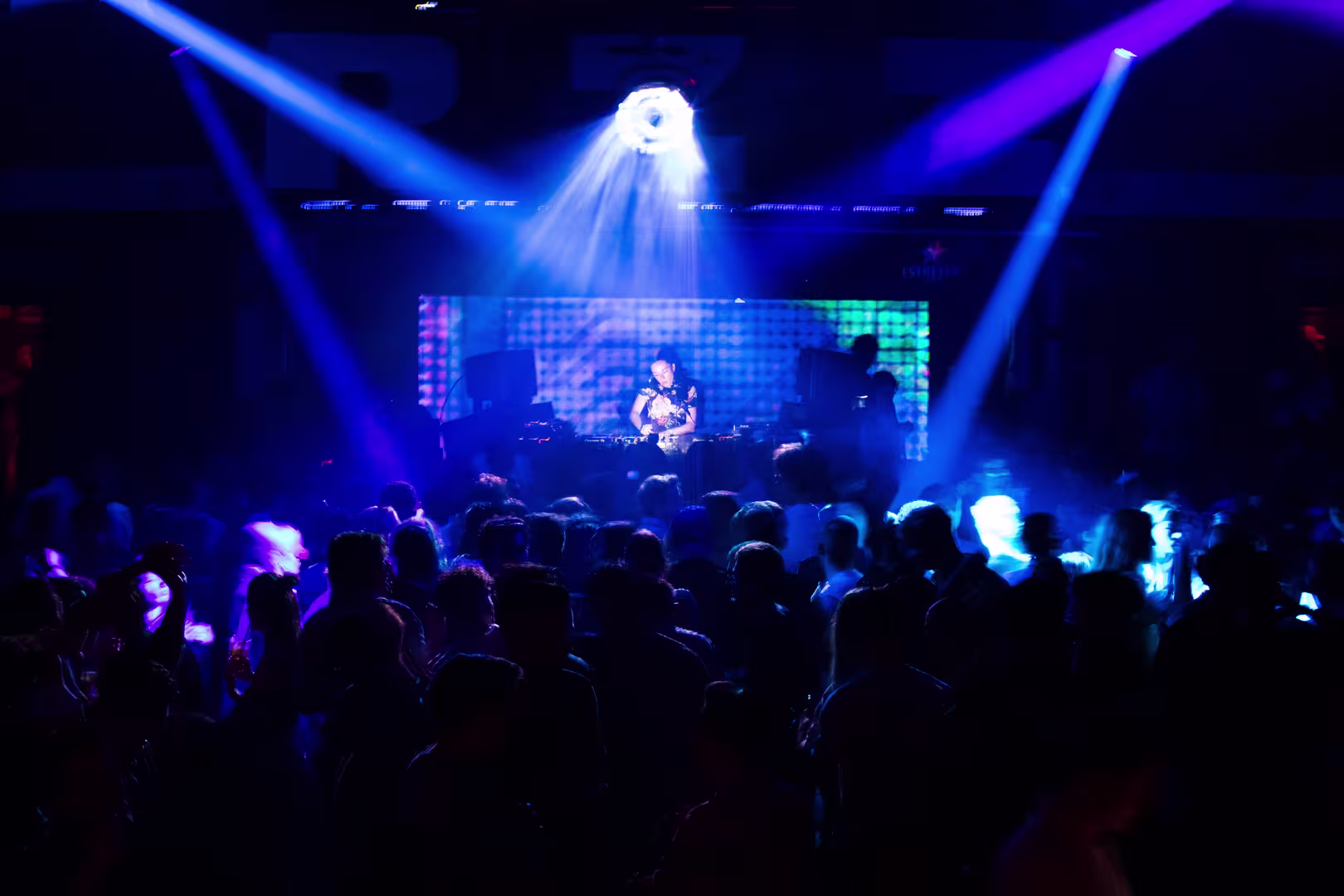 Ambiente de fiesta animado en Razzmatazz, con luces de colores y una multitud disfrutando de la música en vivo mientras el DJ mezcla.