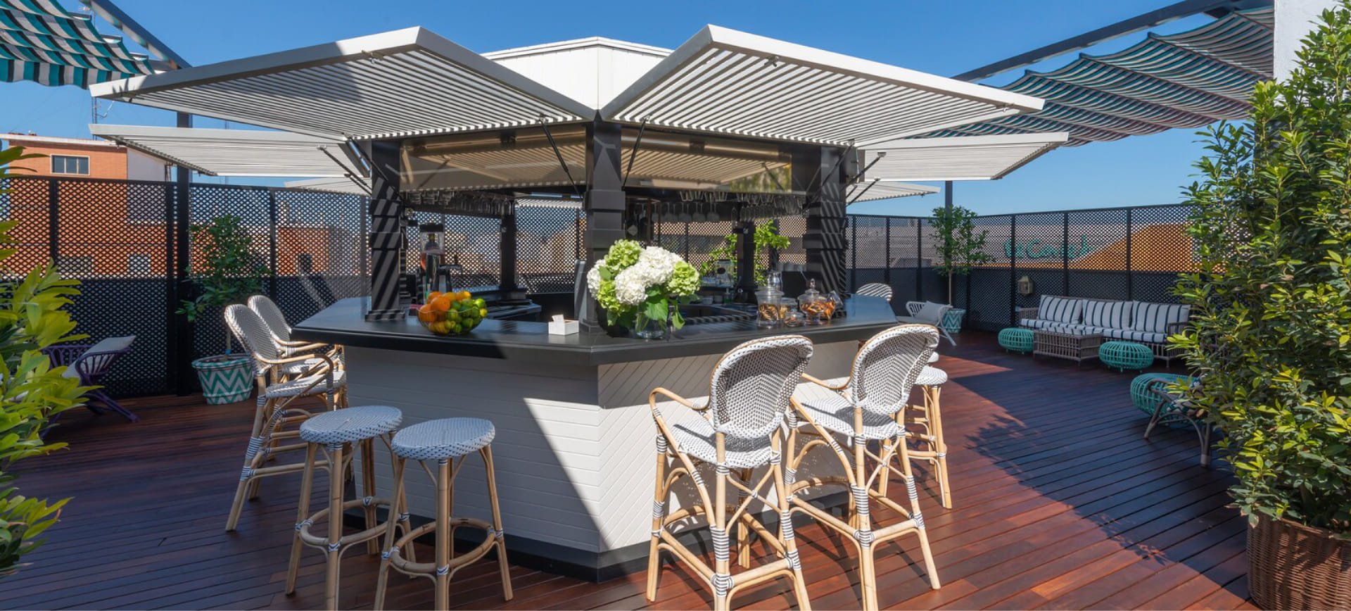 Rooftop de Kamikaze con barra central cubierta, taburetes de mimbre, decoración tropical y suelos de madera, ideal para cócteles bajo el sol de Valencia.