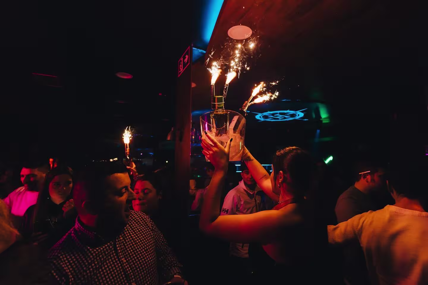 Celebración en Norte by Harbour con botellas y bengalas encendidas. Ambiente animado y festivo en una noche de fiesta.