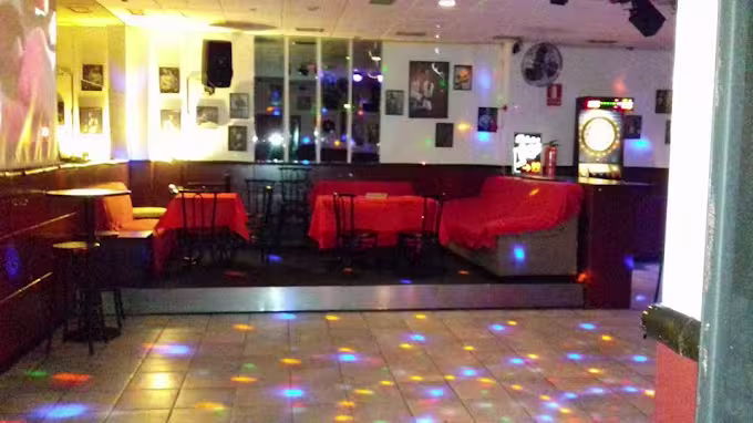 Peter's Bar con mesas iluminadas, diana y luces de colores, creando un ambiente relajado y divertido para disfrutar con amigos.