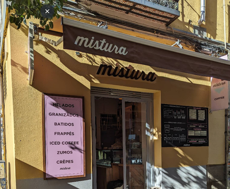 Exterior de Mistura en Augusto Figueroa con toldo marrón, cartel rosa y menú visible desde la entrada en una fachada de color ocre.