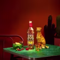 La imagen muestra una botella de vodka Smirnoff Spicy Tamarind, un estatuilla de un jaguar y unos shots de vodka.