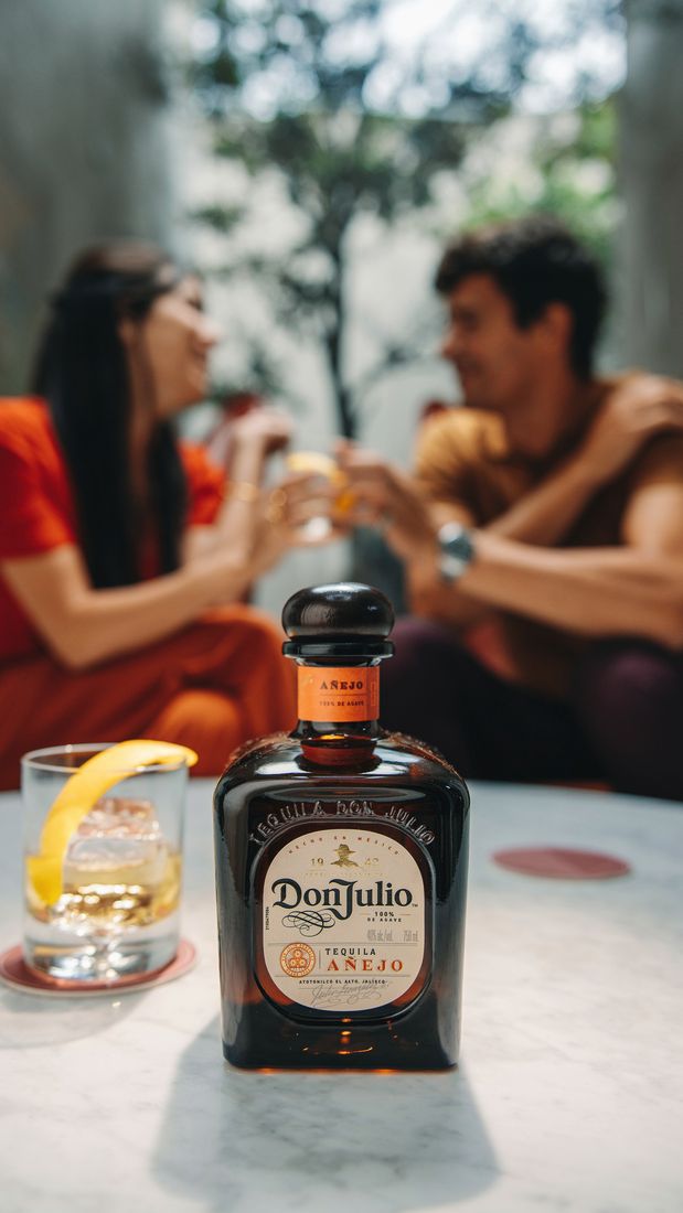 La imagen muestra a una persona agarrando una botella de ron Zacapa 23 y colocando una rodaja de naranja en un vaso que contiene el cóctel Old Fashioned.