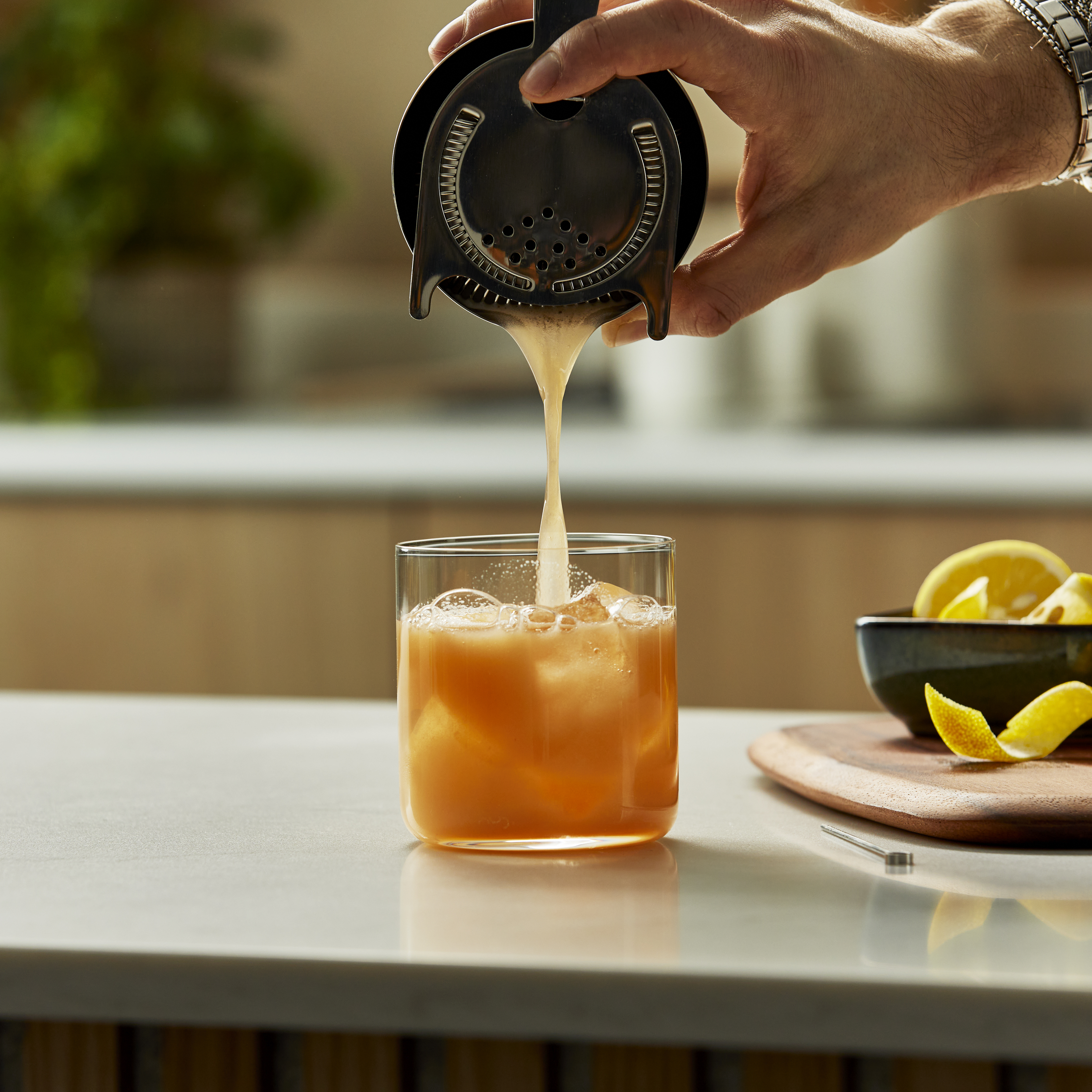 Someone pouring a sour cocktail through a strainer into a rocks glass