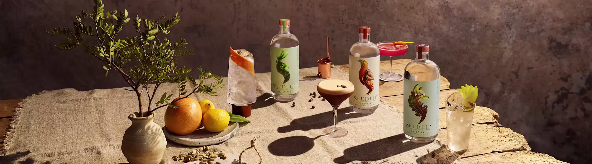 Seedlip bottles and non-alcoholic cocktails arranged on a rustic table with fresh fruit and plants