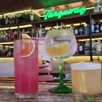 En la imagen se ven 3 cócteles y de fondo la barra del lugar. En el costado izquierdo una botella de Tequila Don Julio.