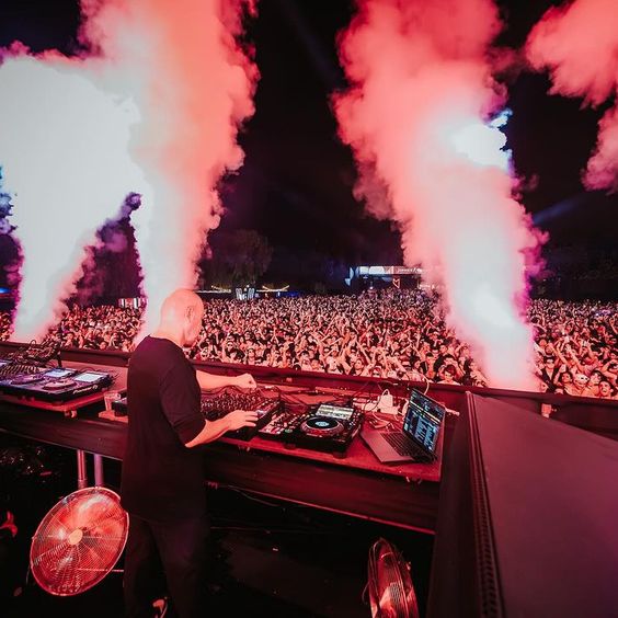 La imagen muestra la fiesta "Music On", con un DJ y un grupo grande de personas.