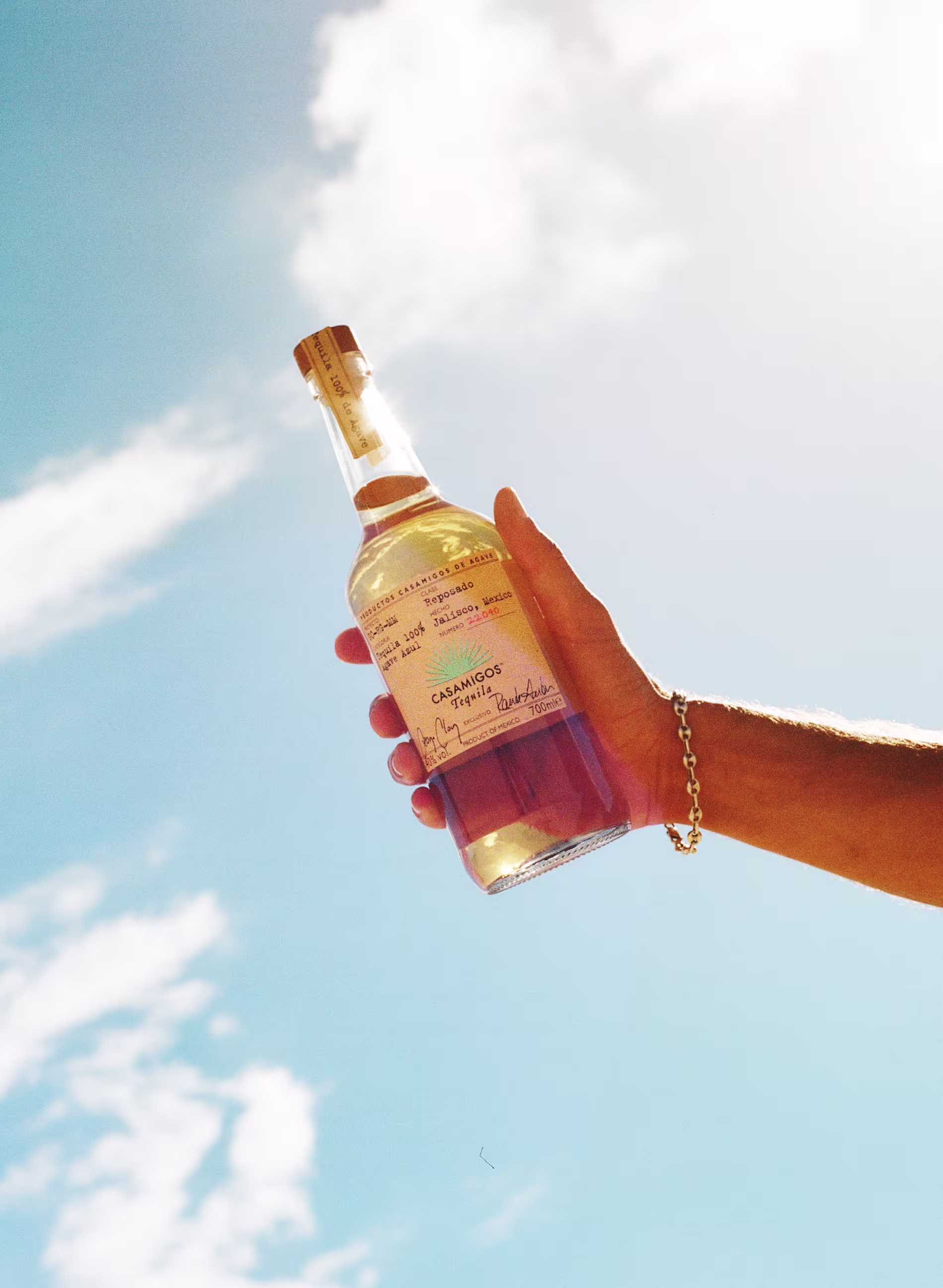 Hand holding a bottle of Casamigos Tequila Reposado against a bright blue sky