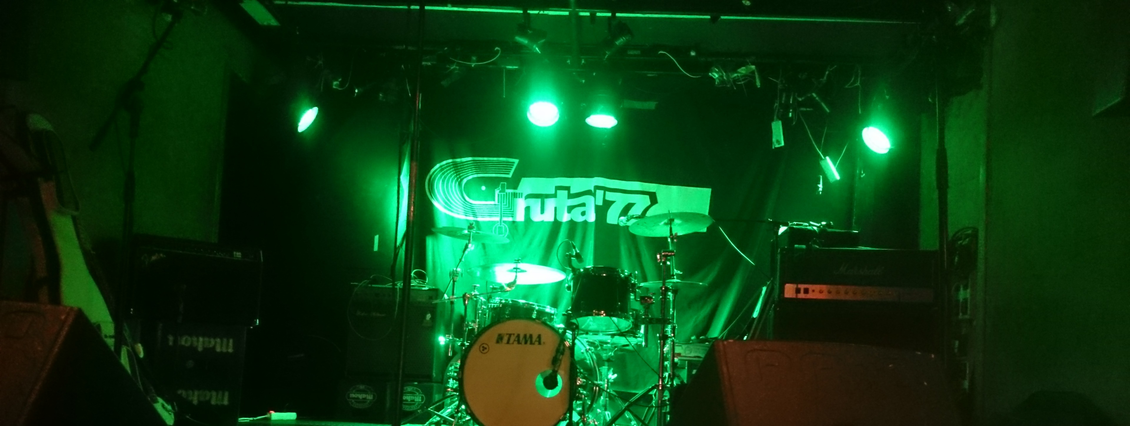Gruta 77 es un local underground con escenario verde vibrante, batería central y amplificadores, ideal para conciertos de rock y punk.
