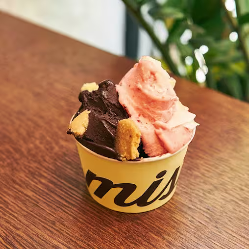 Tarrina de helado en Mistura calle de Toledo con dos sabores artesanos y trozos de galleta sobre una mesa de madera.