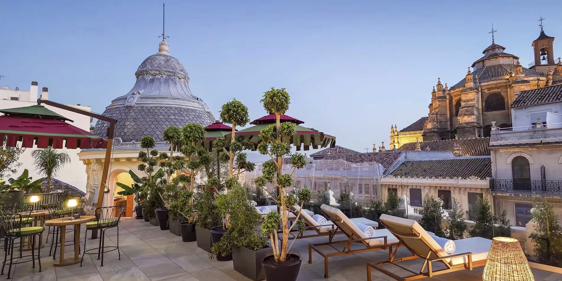 La imagen muestra la elegante terraza de "Terraza Miralba", con tumbonas rodeadas de vegetación y sombrillas, ofreciendo vistas impresionantes.